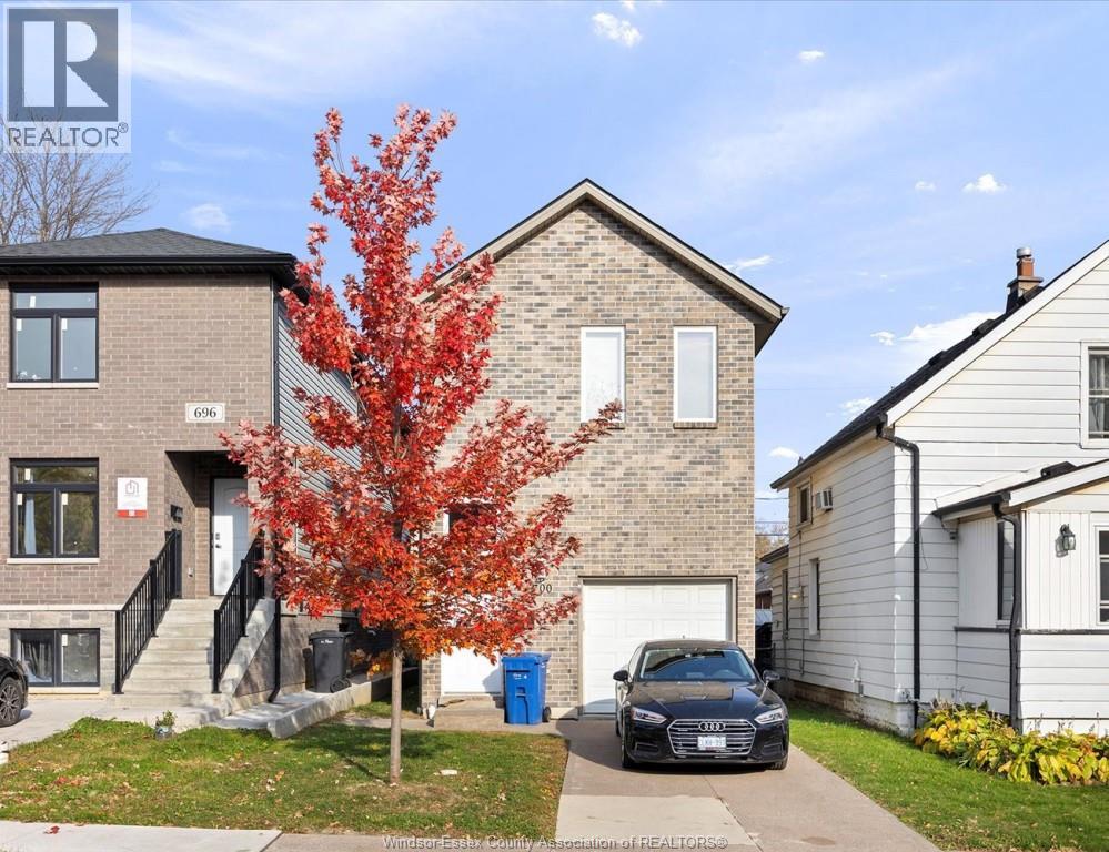 A tree with red leaves is in front of a brick house with a car parked in front of it.