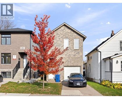 A tree with red leaves is in front of a brick house with a car parked in front of it.