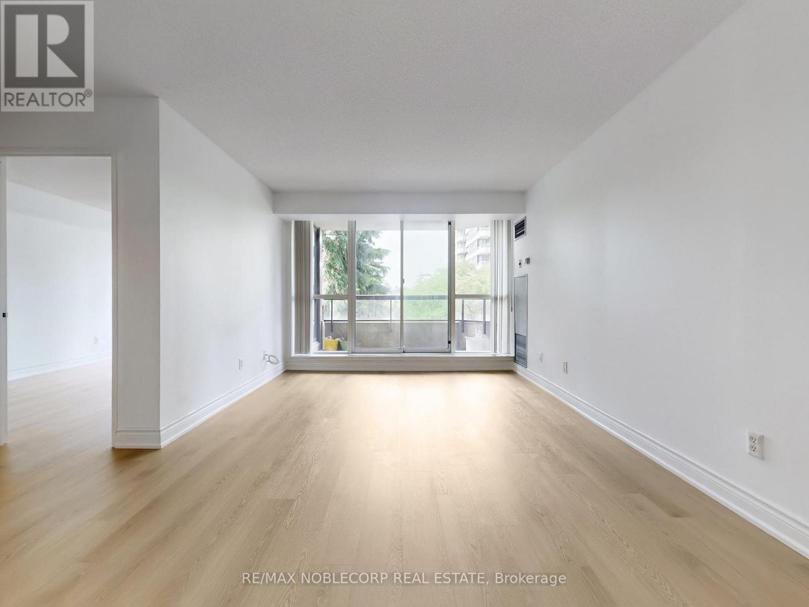 A spacious room with wooden flooring and a sliding glass door leading to a balcony.