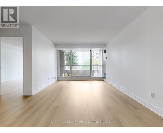 A spacious room with wooden flooring and a sliding glass door leading to a balcony.