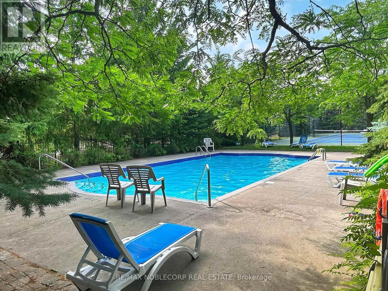 A pool surrounded by trees and chairs.