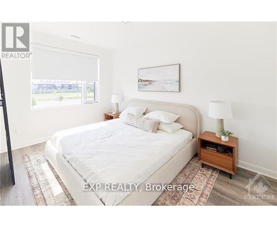 A bedroom with a large bed, a nightstand with a lamp, and a framed picture on the wall.