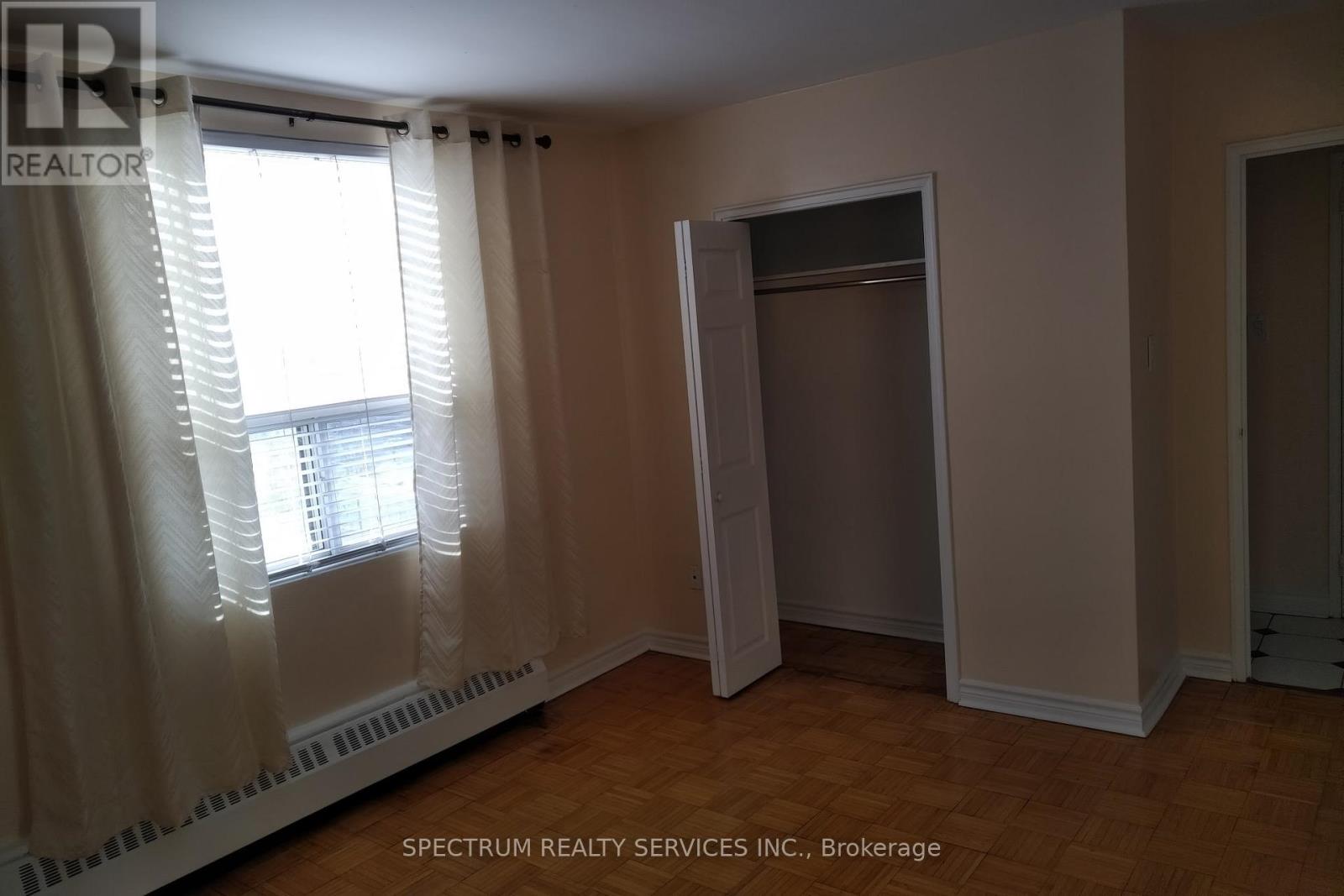 A room with a window covered by white curtains and a door on the right side.