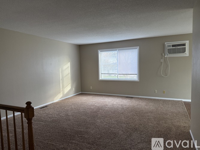 A room with a carpeted floor, a window with blinds, and an air conditioning unit on the wall.