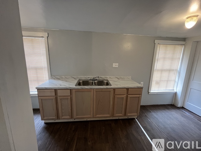 A kitchen island with a sink is in the middle of a room with wood floors and white walls.