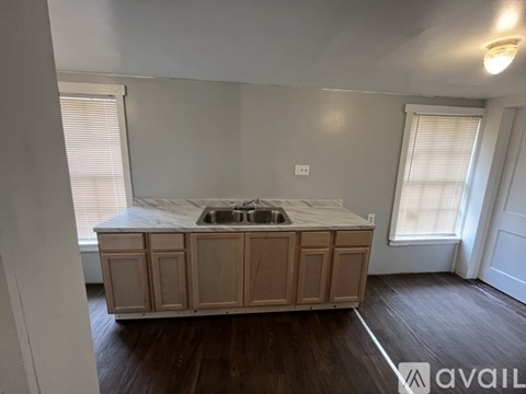A kitchen island with a sink is in the middle of a room with wood floors and white walls.