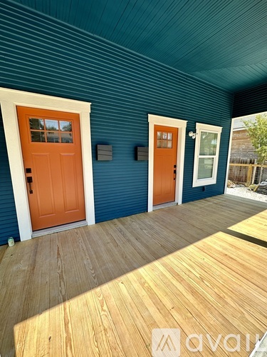 A blue house with two orange doors and a wooden deck.