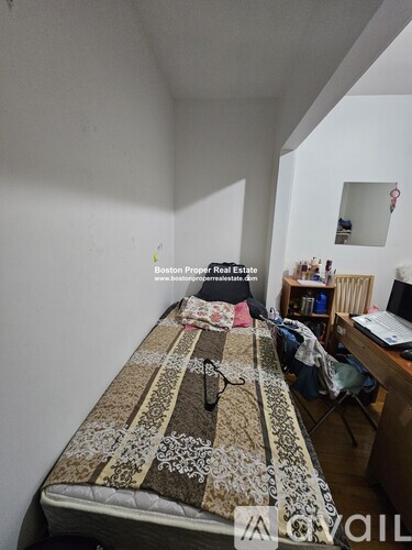 A bedroom with a bed covered in a patterned comforter, a desk with a laptop, and a chair.