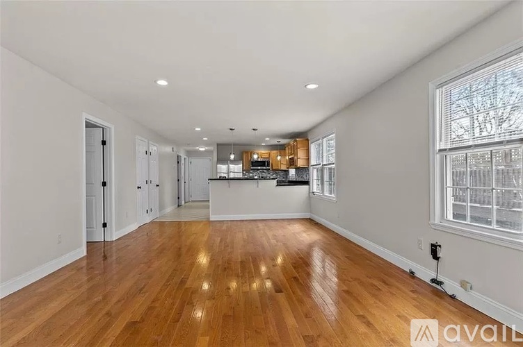 A spacious room with wooden flooring and a kitchen area in the background.
