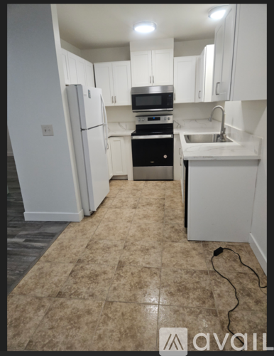 A kitchen with white cabinets and appliances, a sink, and a tiled floor.