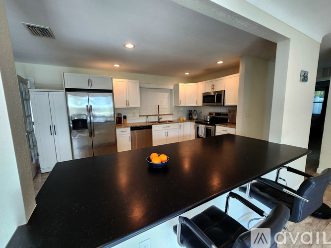 A kitchen with a black countertop and a bowl of oranges on it.