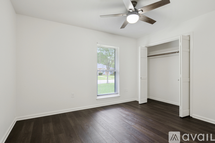 A room with a ceiling fan and a window with a view of a lawn and trees outside.