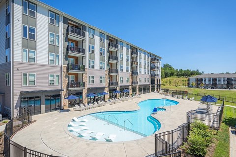 A large swimming pool is surrounded by a black fence in front of apartment buildings.