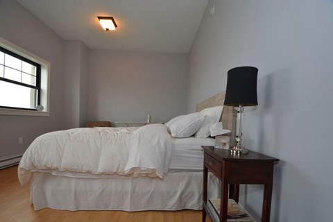 A bedroom with a white bed and a black lamp on a wooden table.
