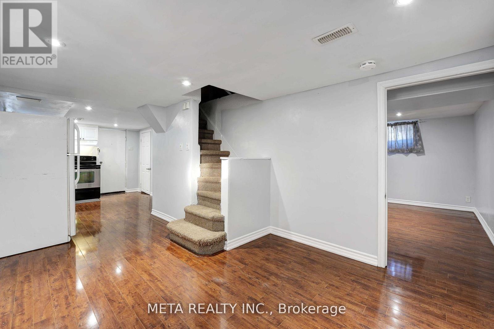 A spacious room with wooden floors and a staircase in the middle.