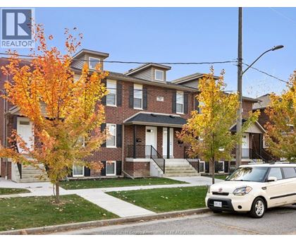 A white car is parked in front of a brick house.