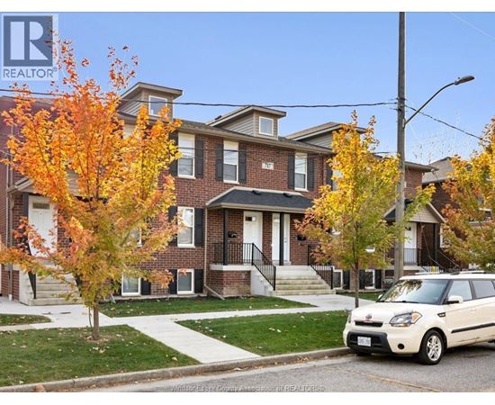A white car is parked in front of a brick house.