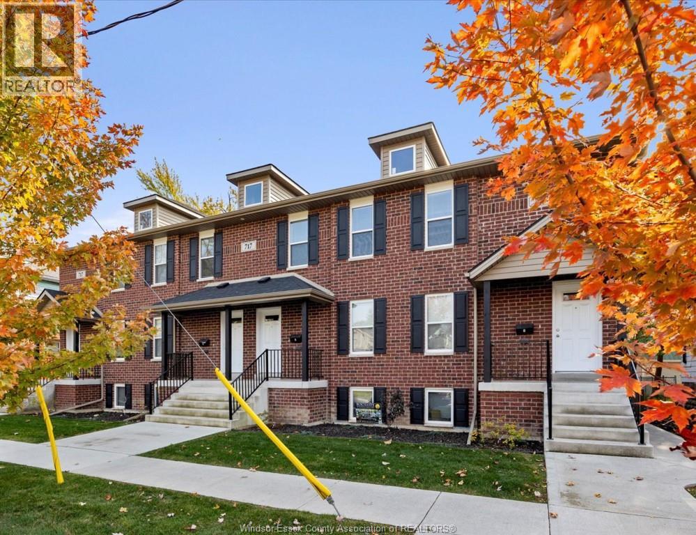 A house with a red brick facade and a white door is surrounded by trees with orange leaves.