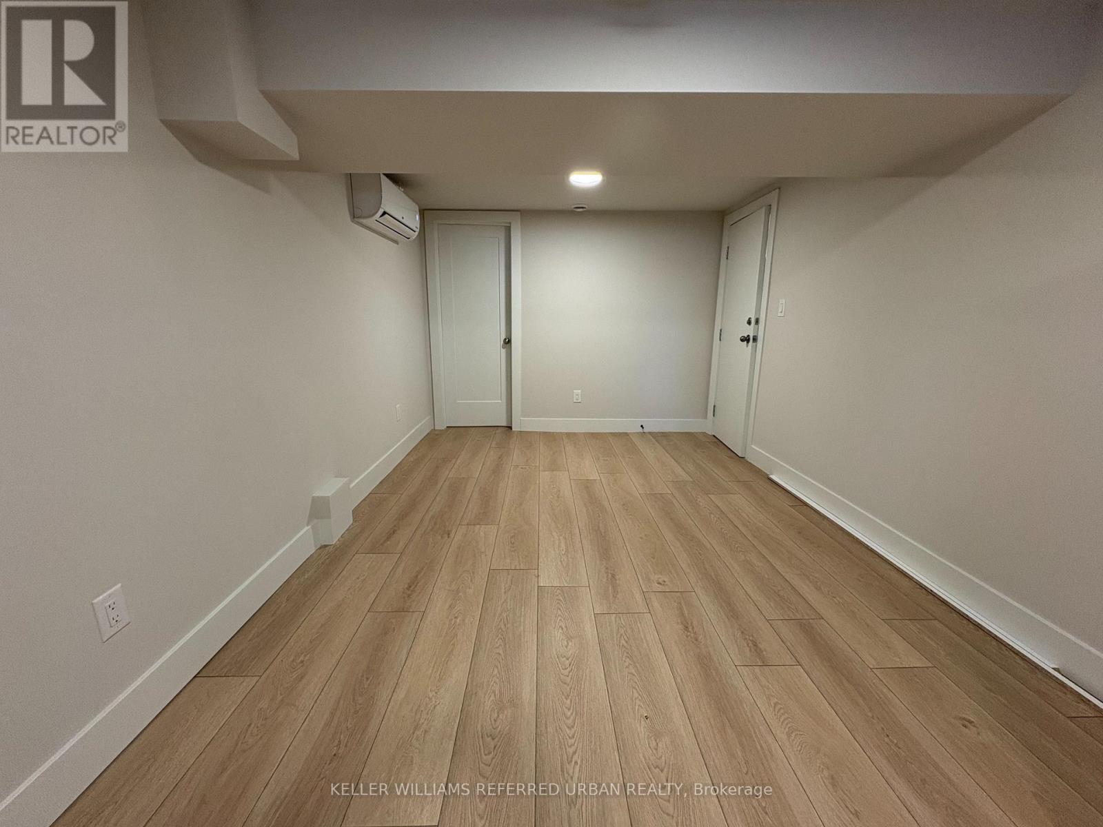 A spacious room with wooden flooring and white walls.