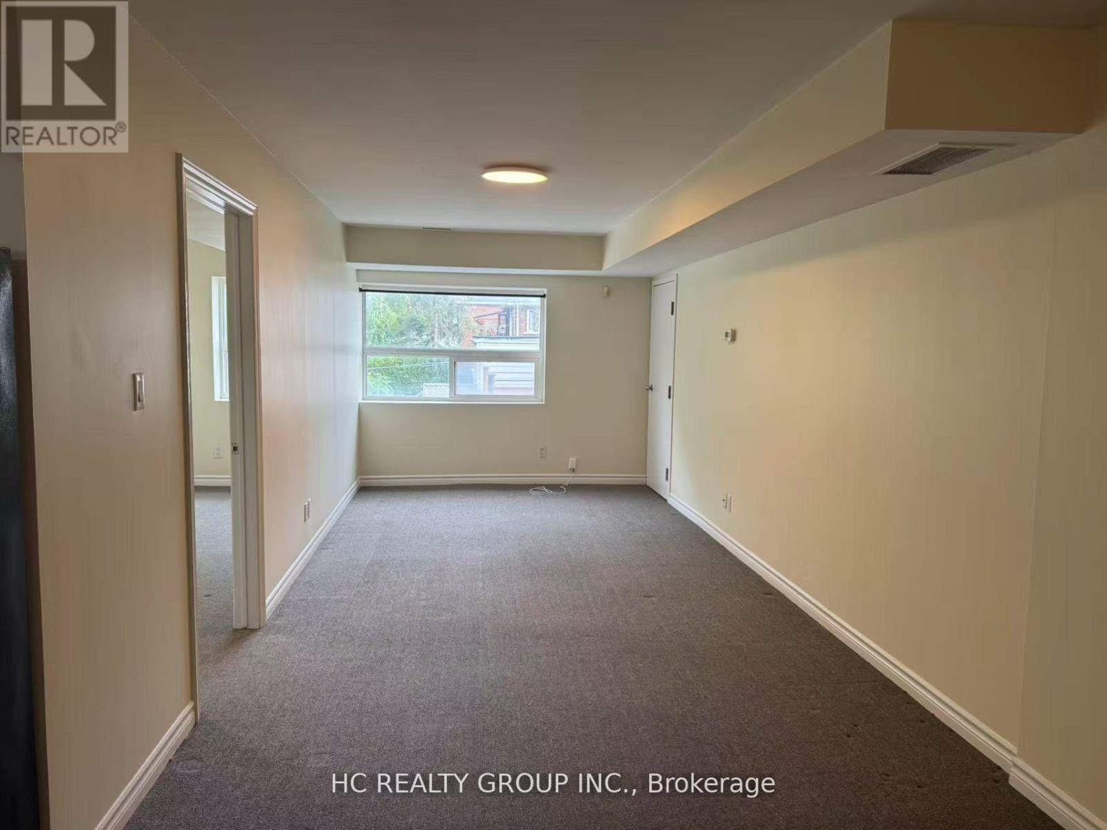 A room with a carpeted floor and a window with a view of trees and houses outside.