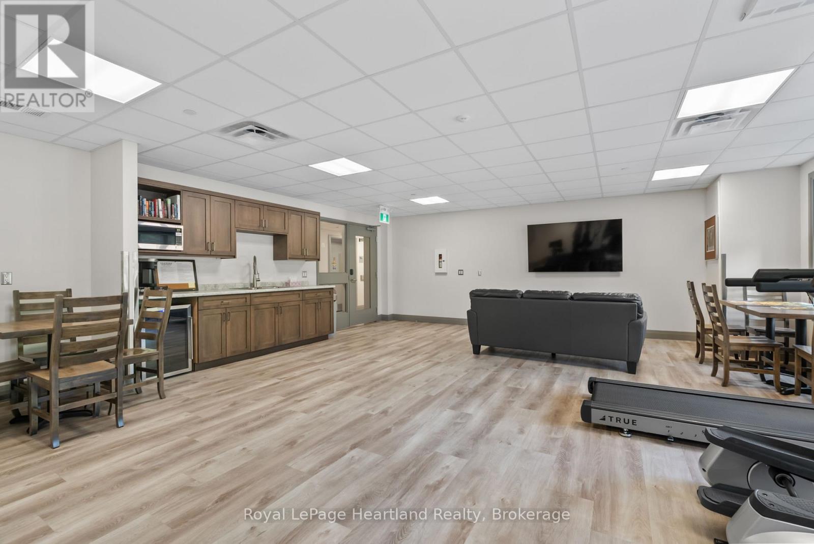 A spacious room with wooden flooring and furniture including a couch, chairs, and a dining table.