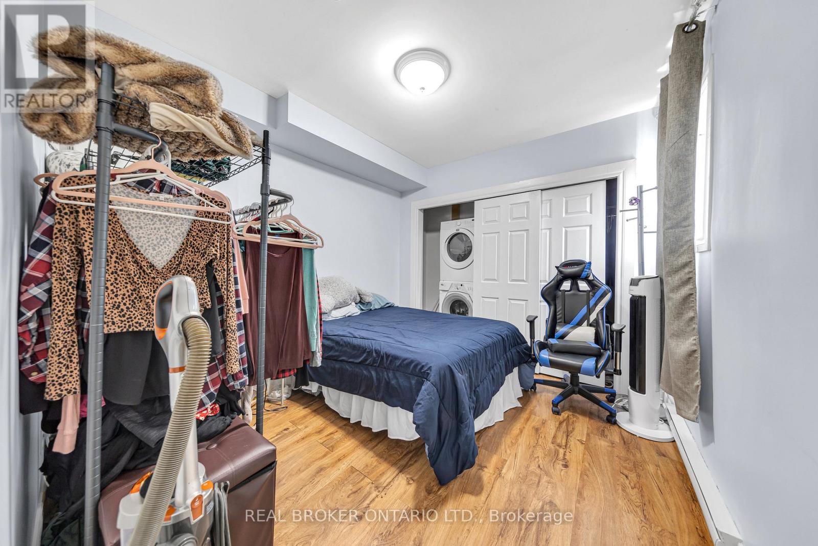 A bedroom with a bed, a chair, and a closet with clothes hanging.