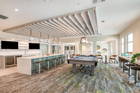 A billiard table is in the middle of a room with a bar and a kitchen.