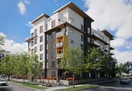 A modern multi-story apartment building with balconies and trees in front.