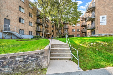 A stone wall borders a grassy area in front of apartment buildings.