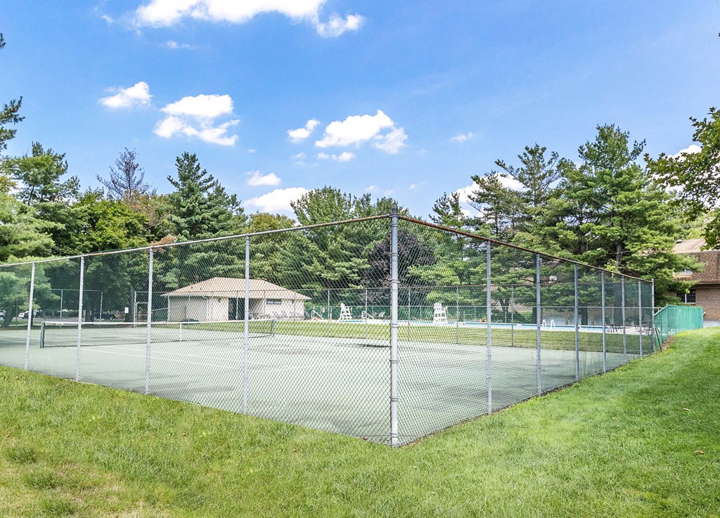 a fenced in tennis court with a house in the background