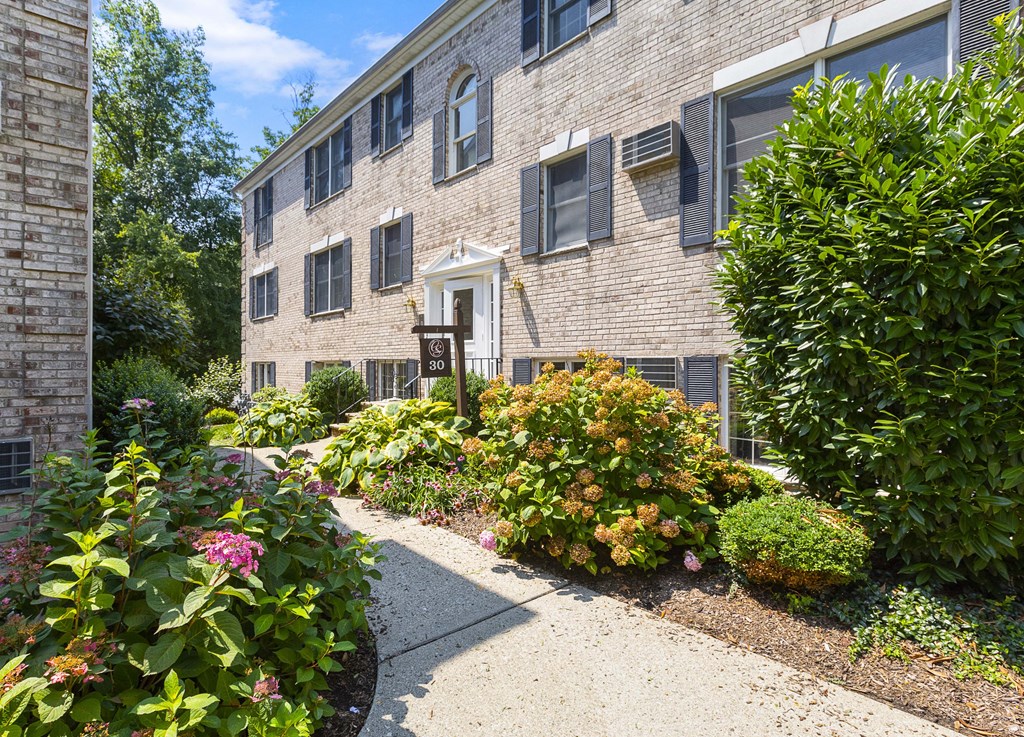 an exterior view of a brick apartment building with a sidewalk and gardens