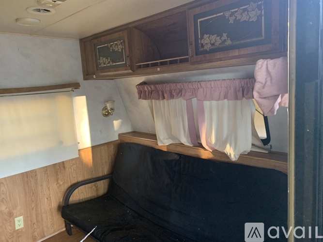 A black couch sits in a room with a wooden cabinet and a window with curtains.