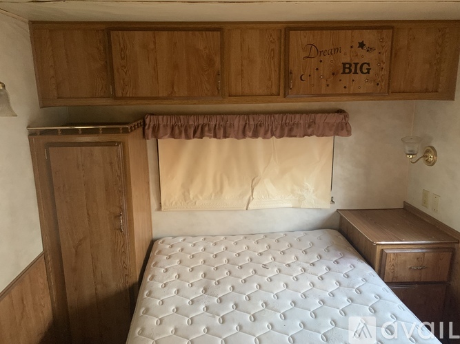 A bedroom with a bed, wooden cabinets, and a window with a curtain.