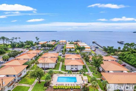 A view of a resort with a pool and a body of water in the background.