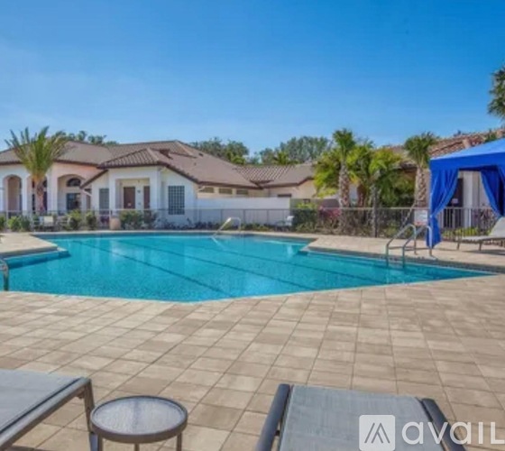A pool surrounded by a tiled patio and a house in the background.