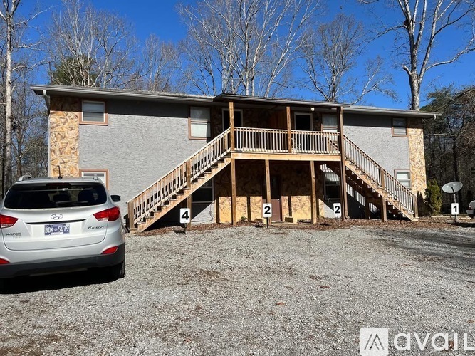 A silver car is parked in front of a two-story house with a wooden deck.
