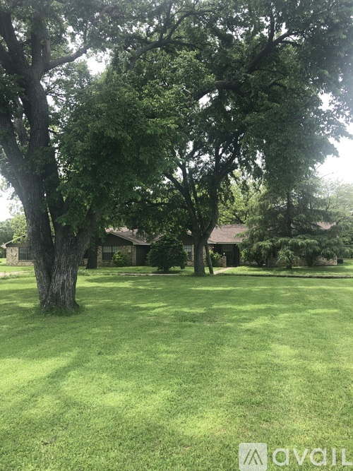 A grassy area with trees and a house in the background.