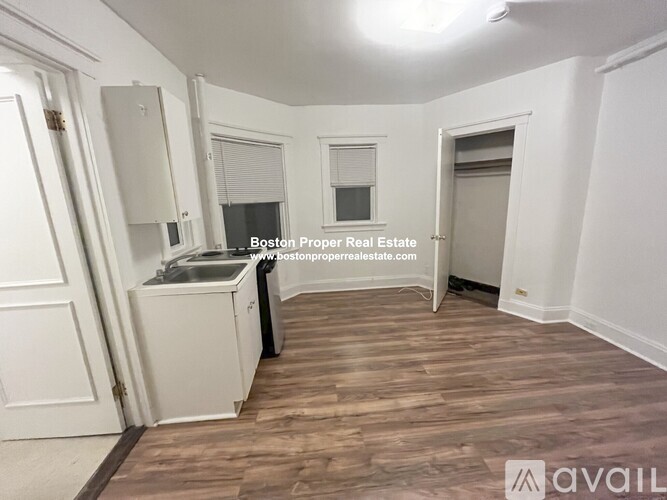 A room with wooden flooring and white walls, featuring a sink and a window.