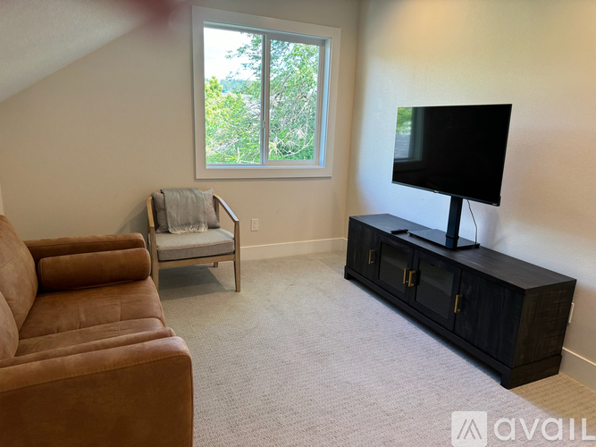A living room with a brown leather couch, a chair, a television, and a cabinet.