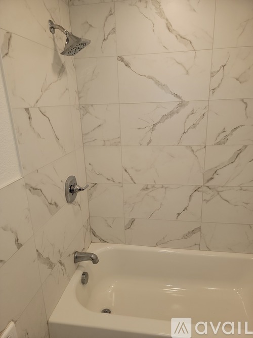 A white marble tiled bathroom with a white bathtub and shower head.
