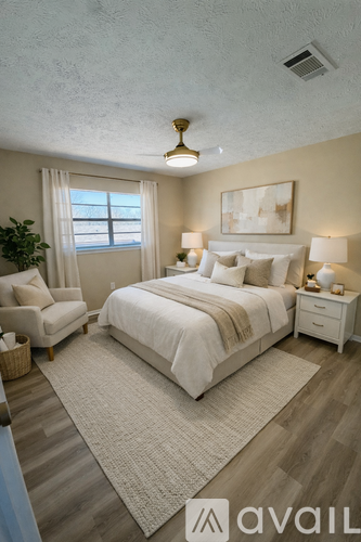 A well-lit bedroom with a large bed, a nightstand, a chair, and a painting on the wall.