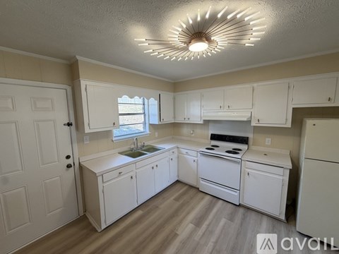 A kitchen with white cabinets and appliances, a window, and a wooden floor.