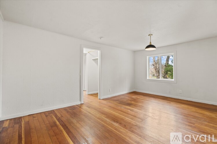A room with wooden floors and white walls, with a window showing trees outside.
