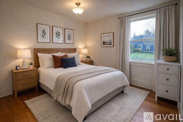 A bedroom with a large bed, two nightstands, and a window with a view of a house.