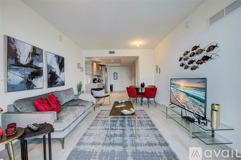 A living room with a grey couch, a coffee table, and a television on the right side.
