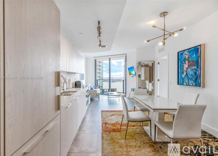 A well-lit, modern kitchen with a dining area and a painting on the wall.