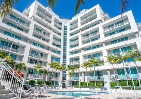 A white building with balconies and palm trees in front.