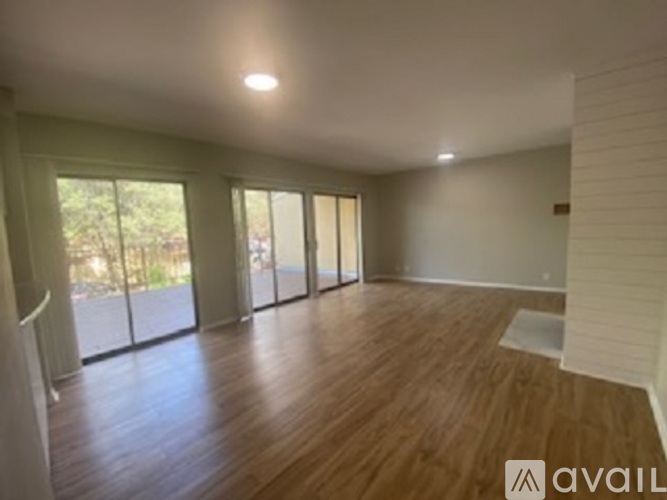 A spacious room with wooden flooring and large windows.