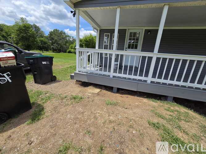 A house with a porch and a trash can in front of it.