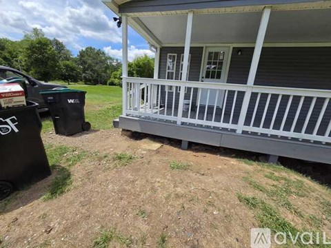 A house with a porch and a trash can in front of it.